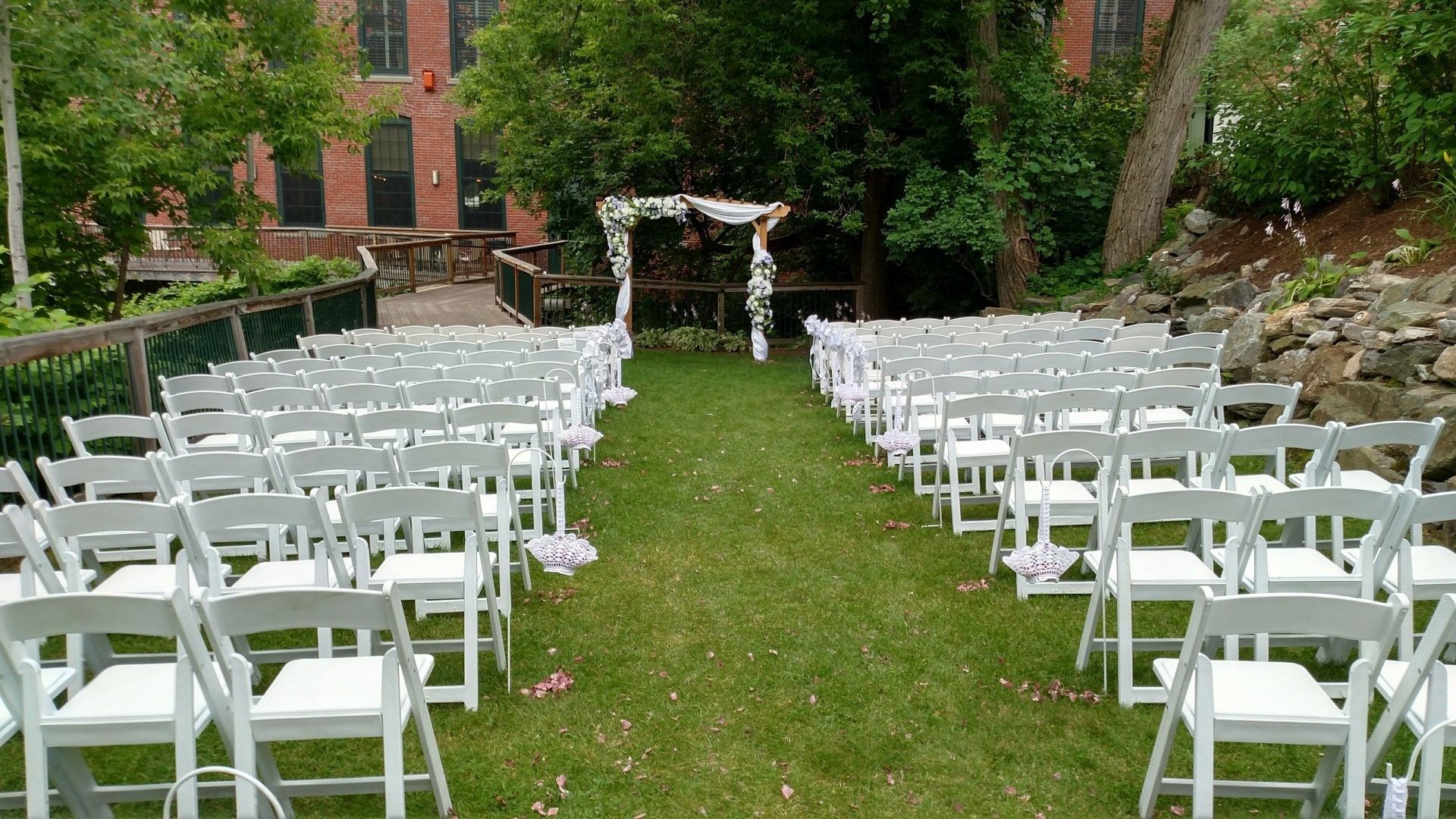 White chairs lined on a grassy aisle leading to a floral wedding arch outdoors