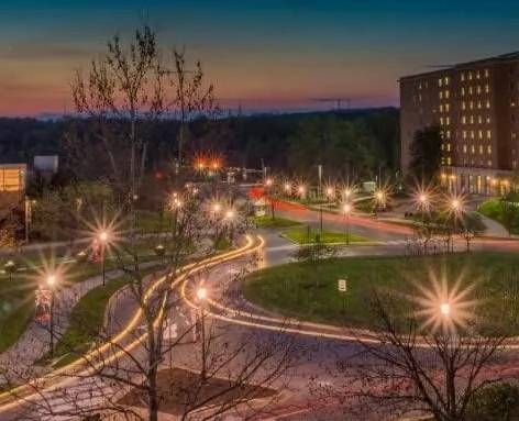 Vista crepuscular de una carretera del campus con estelas de luz de larga exposición provenientes de vehículos y farolas iluminadas.