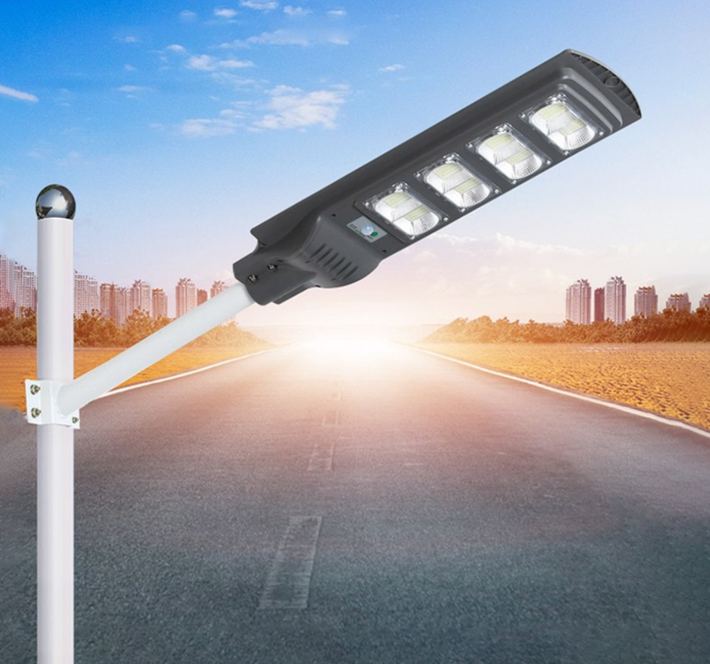 Una farola solar fijada a un poste de metal blanco con una carretera de fondo al atardecer.