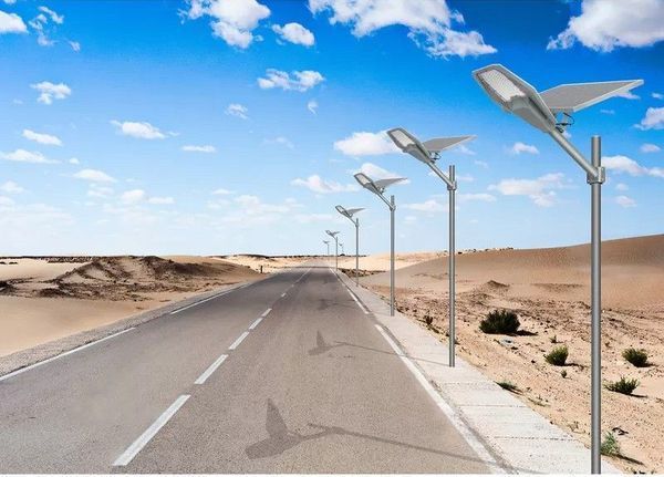 Una hilera de modernas farolas solares bordea una carretera asfaltada que atraviesa un paisaje desértico árido y soleado.