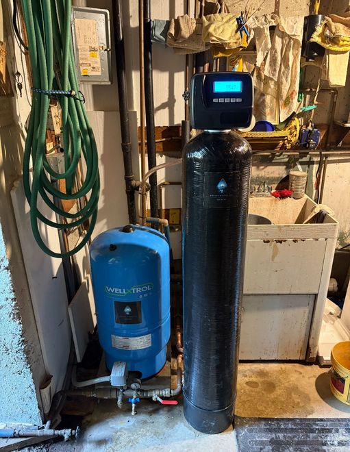 Water filtration system in a basement. Includes a blue pressure tank and tall black tank with a digital display.