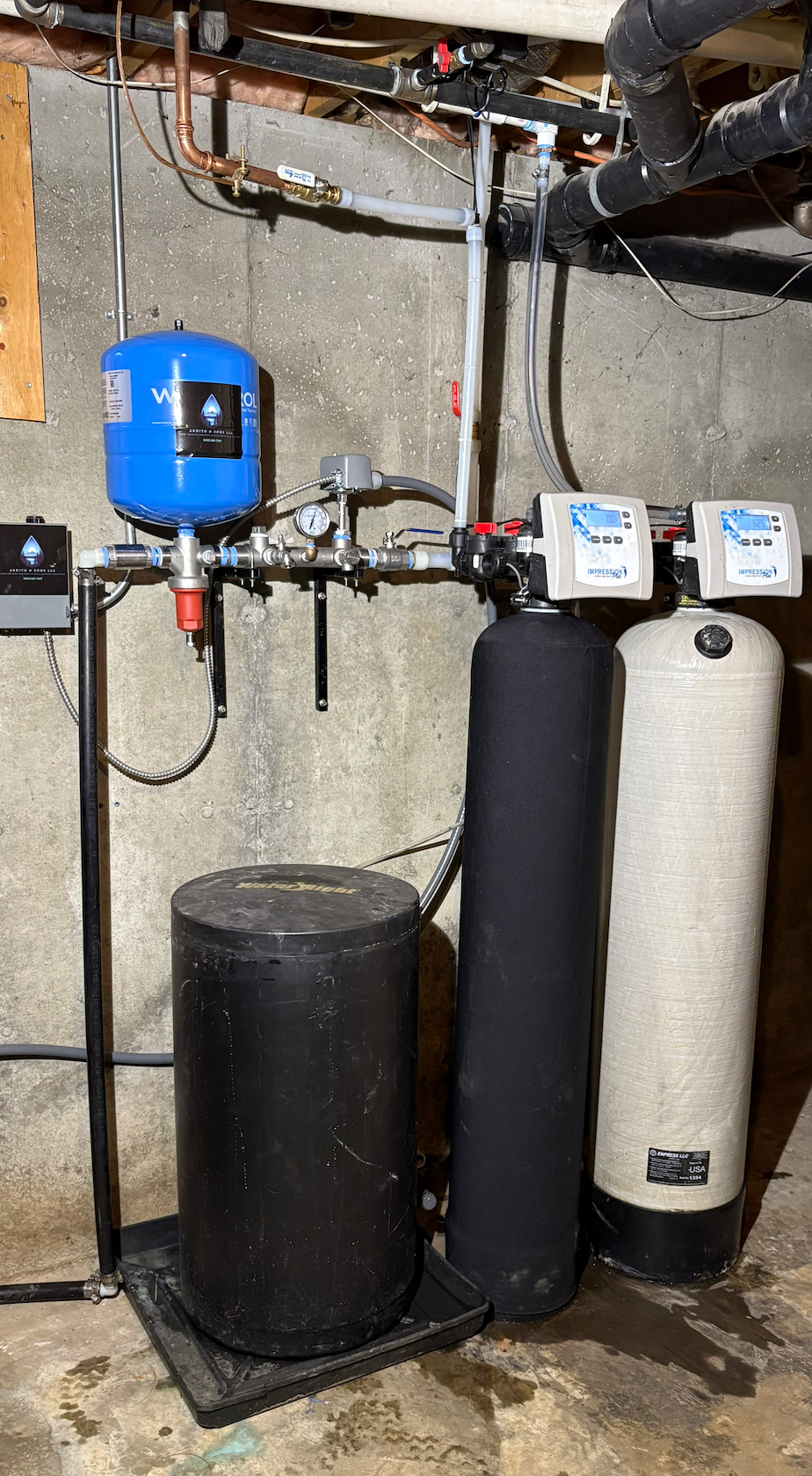 Water filtration system in a basement setting; blue tank, black tanks, pipes.