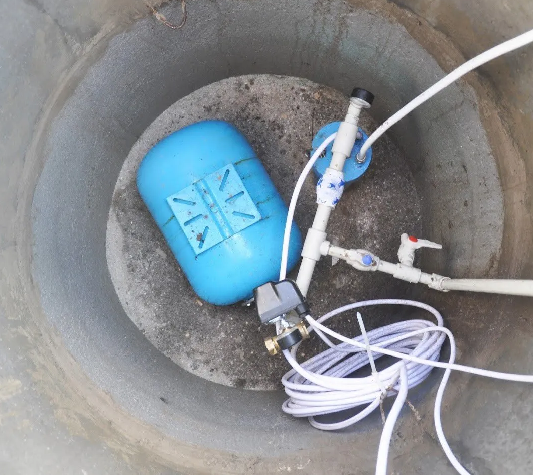 Blue float valve and plumbing inside a concrete cistern.