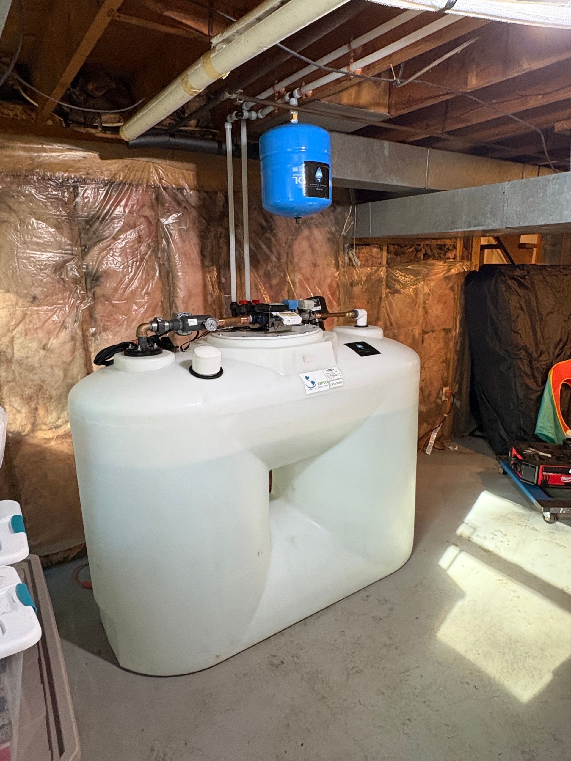 Large white water tank with blue pressure tank in a basement.