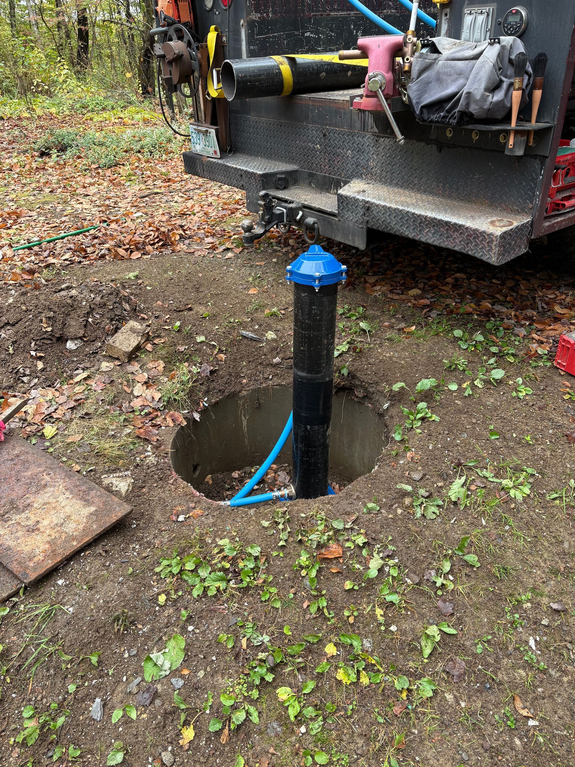 Well with a blue cap, black pipe in an excavation, near a work truck.