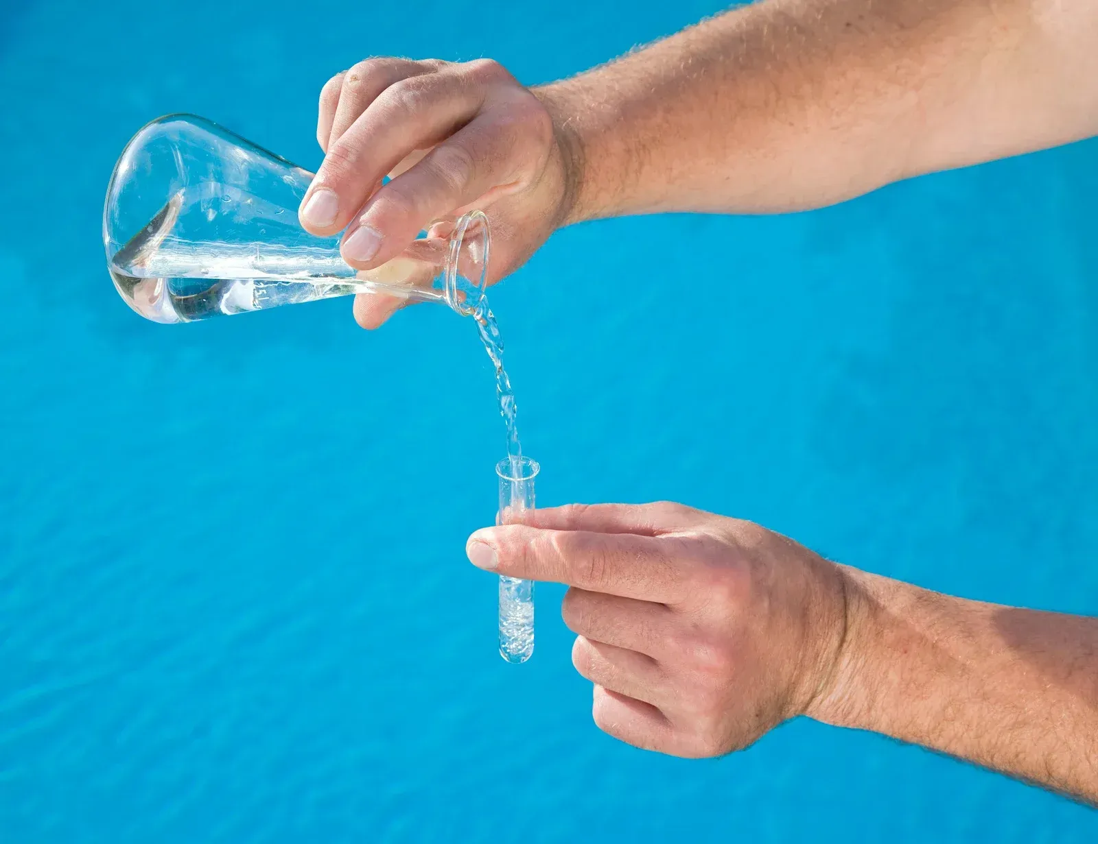 Person pouring liquid from a beaker into a test tube against a blue background.