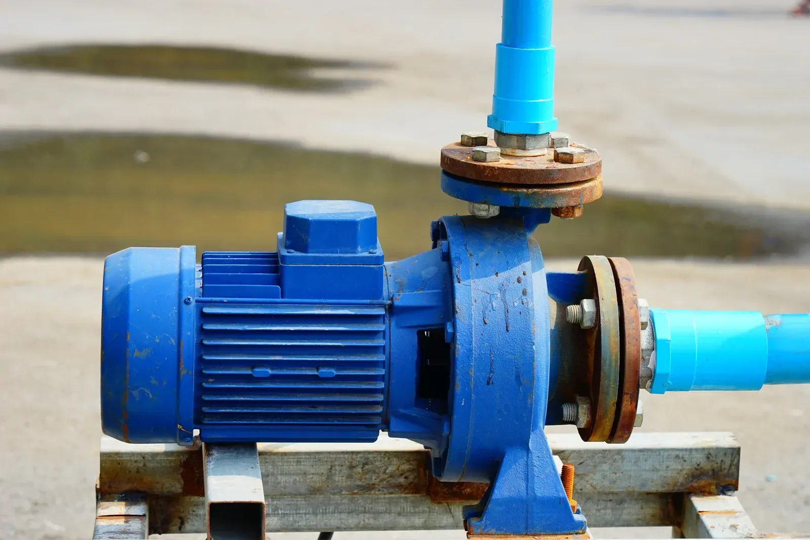 Blue water pump connected to blue pipes, set outdoors on a wooden platform.