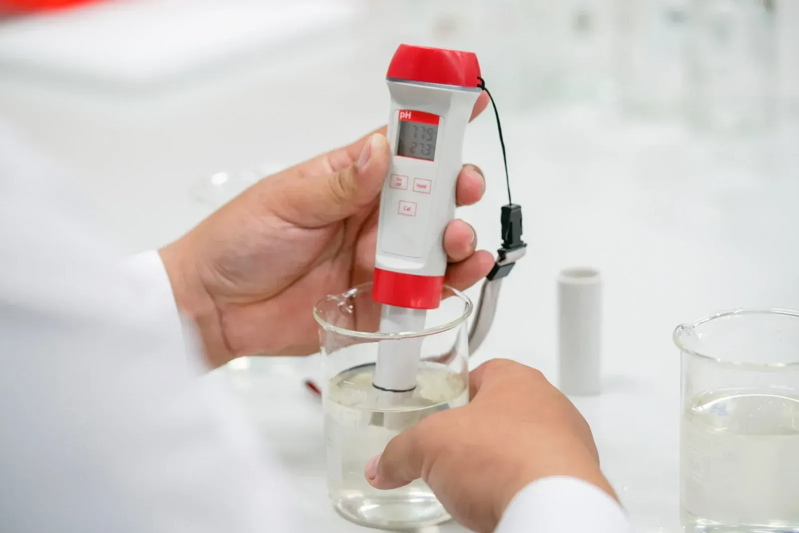 Person testing liquid in a beaker with a pH meter in a lab.