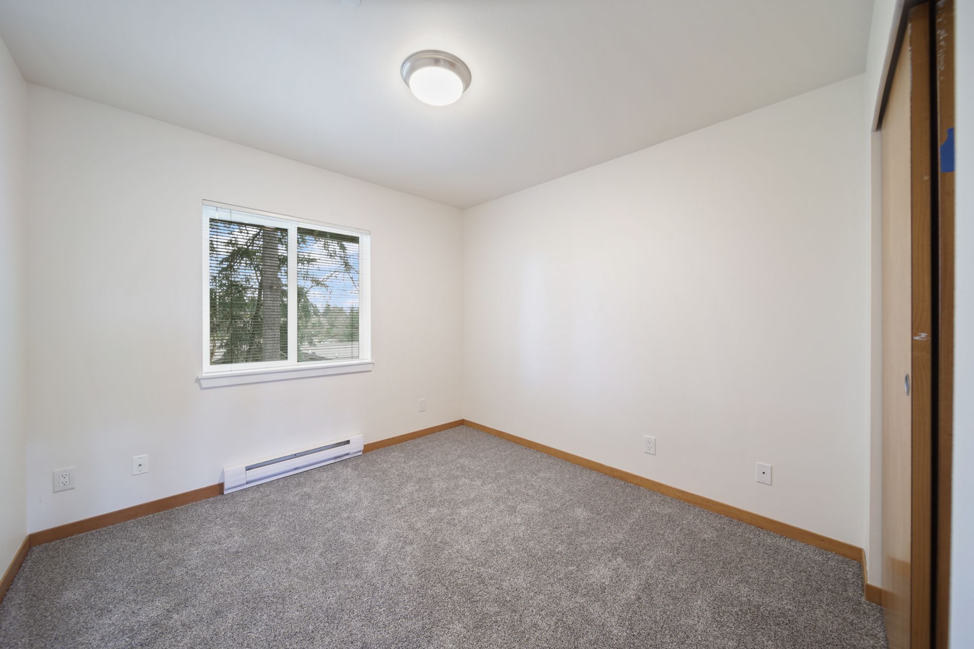 Empty carpeted bedroom with white walls, a window, and a ceiling light