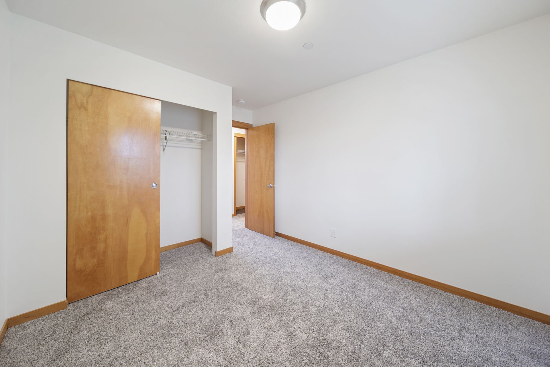 Empty bedroom with beige carpet, white walls, and two wooden closet doors.