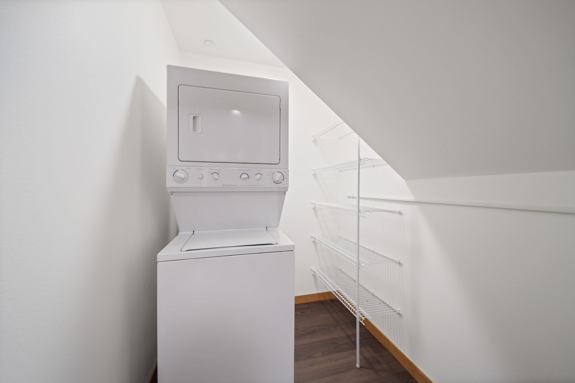 Stacked washer and dryer in a small white laundry nook under a sloped ceiling