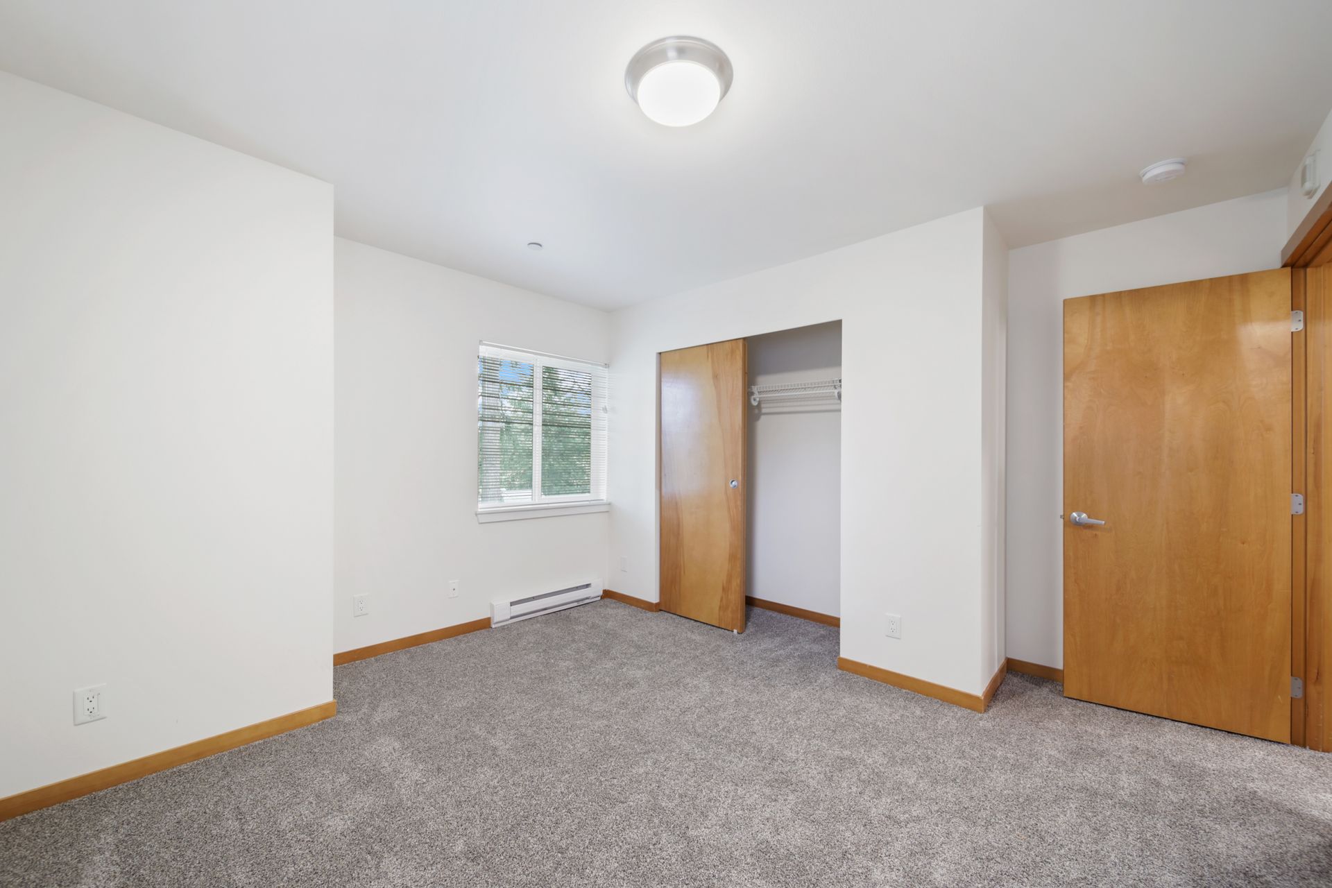 Empty bedroom with white walls, gray carpet, two closets, and a window with blinds