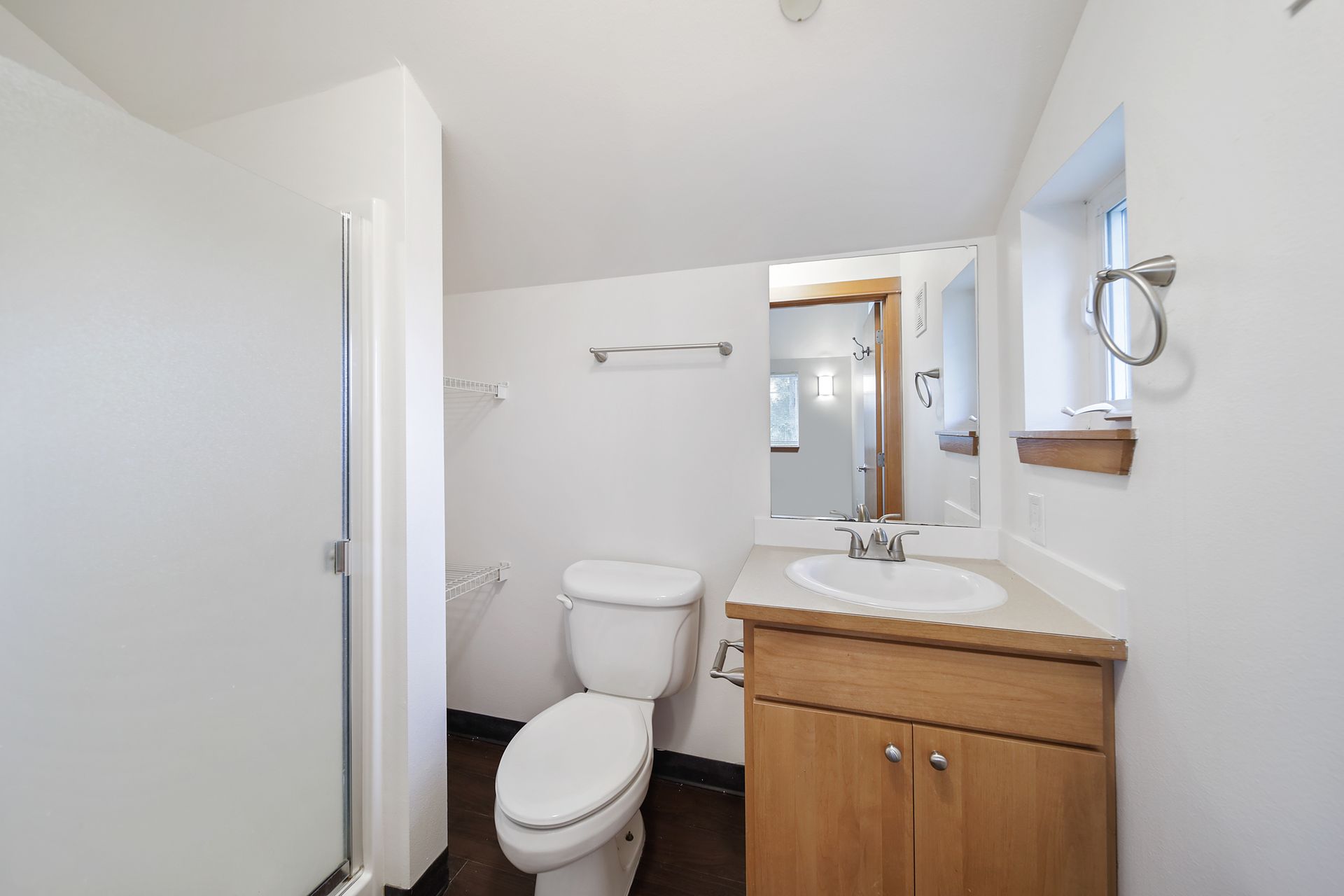 Small bathroom with toilet, wooden vanity, white walls, and shower stall.