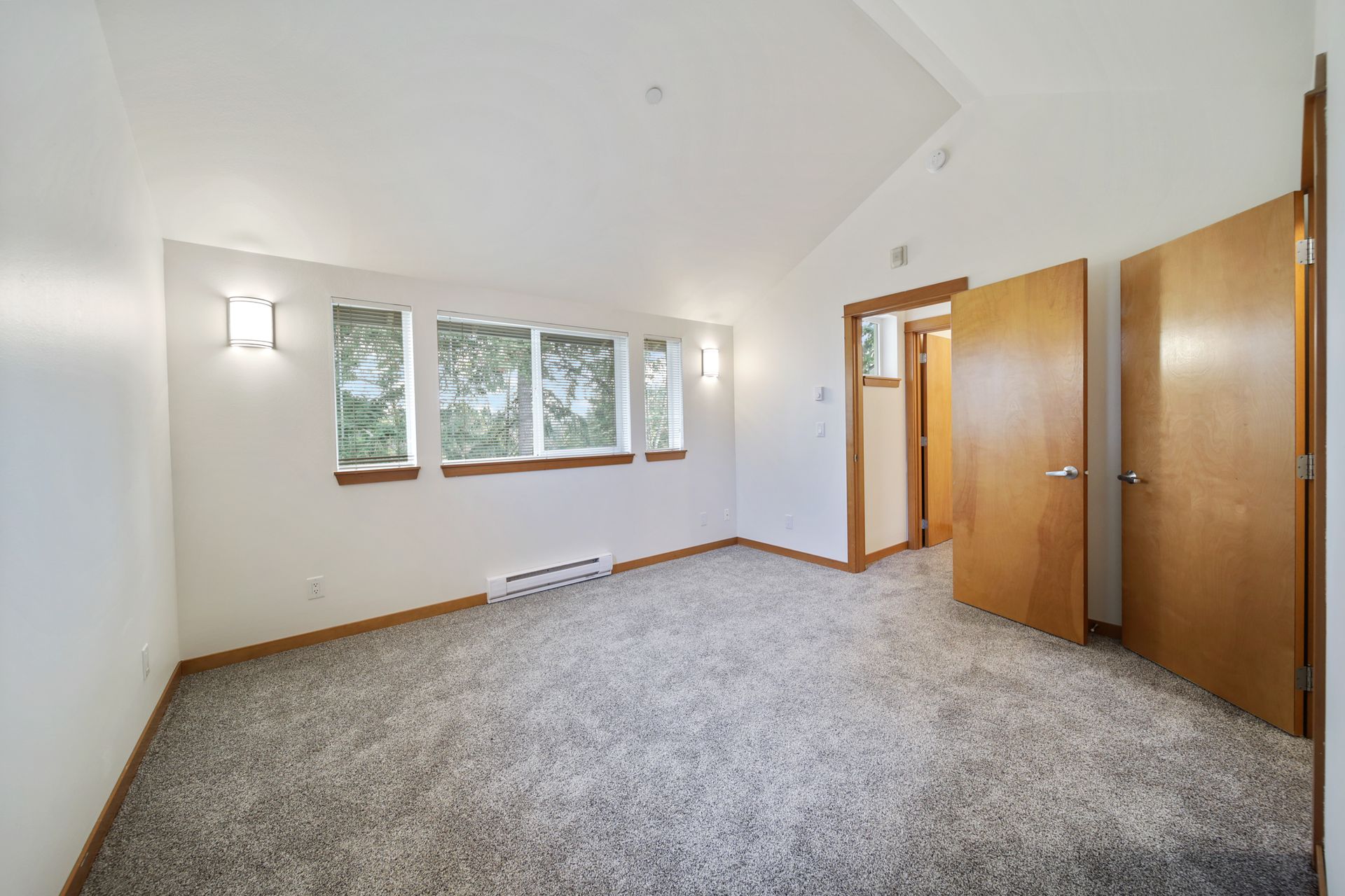 Empty carpeted bedroom with white walls, windows, and open wooden closet doors