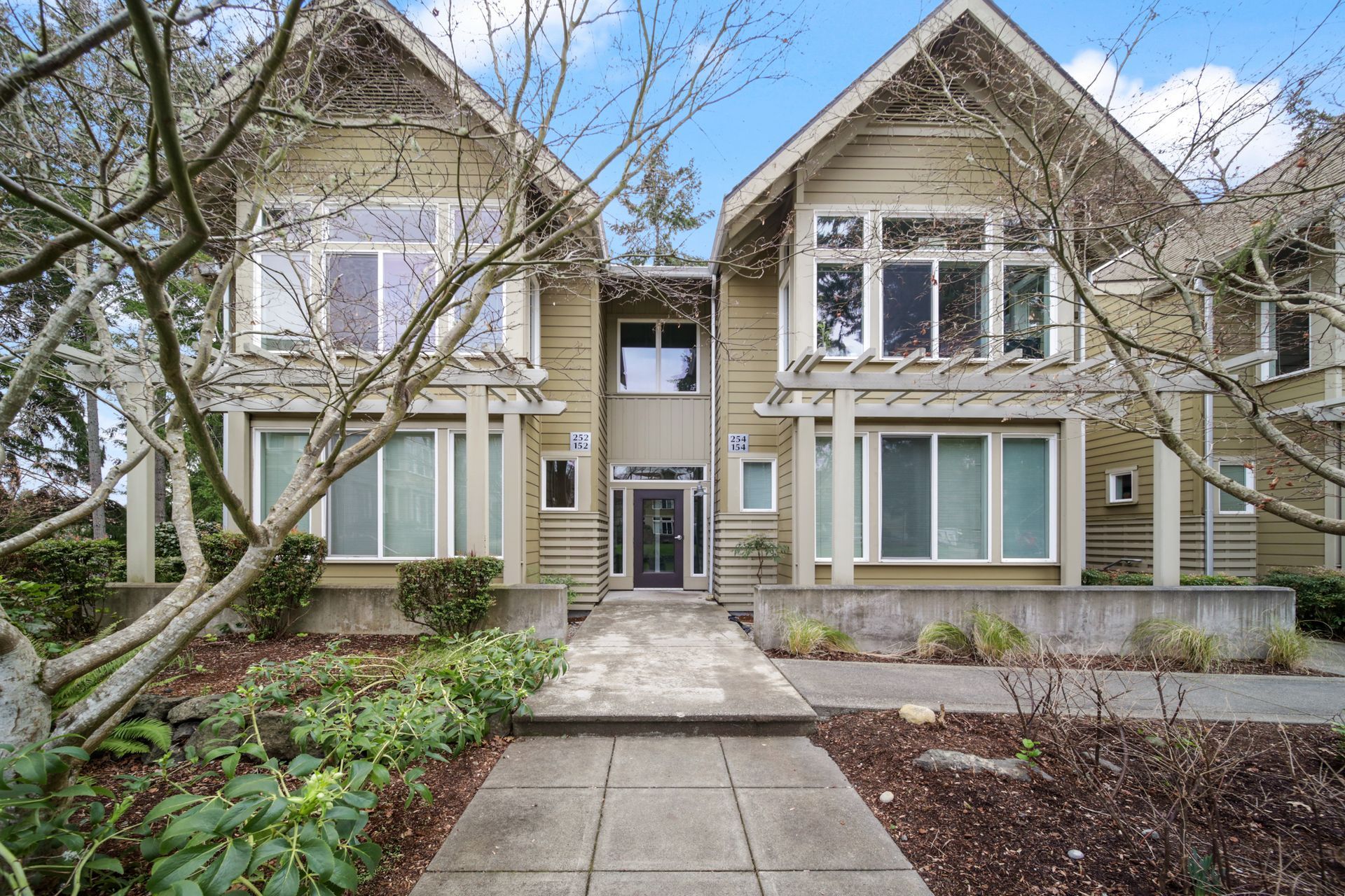 Two beige townhouses with a central walkway and bare trees in front
