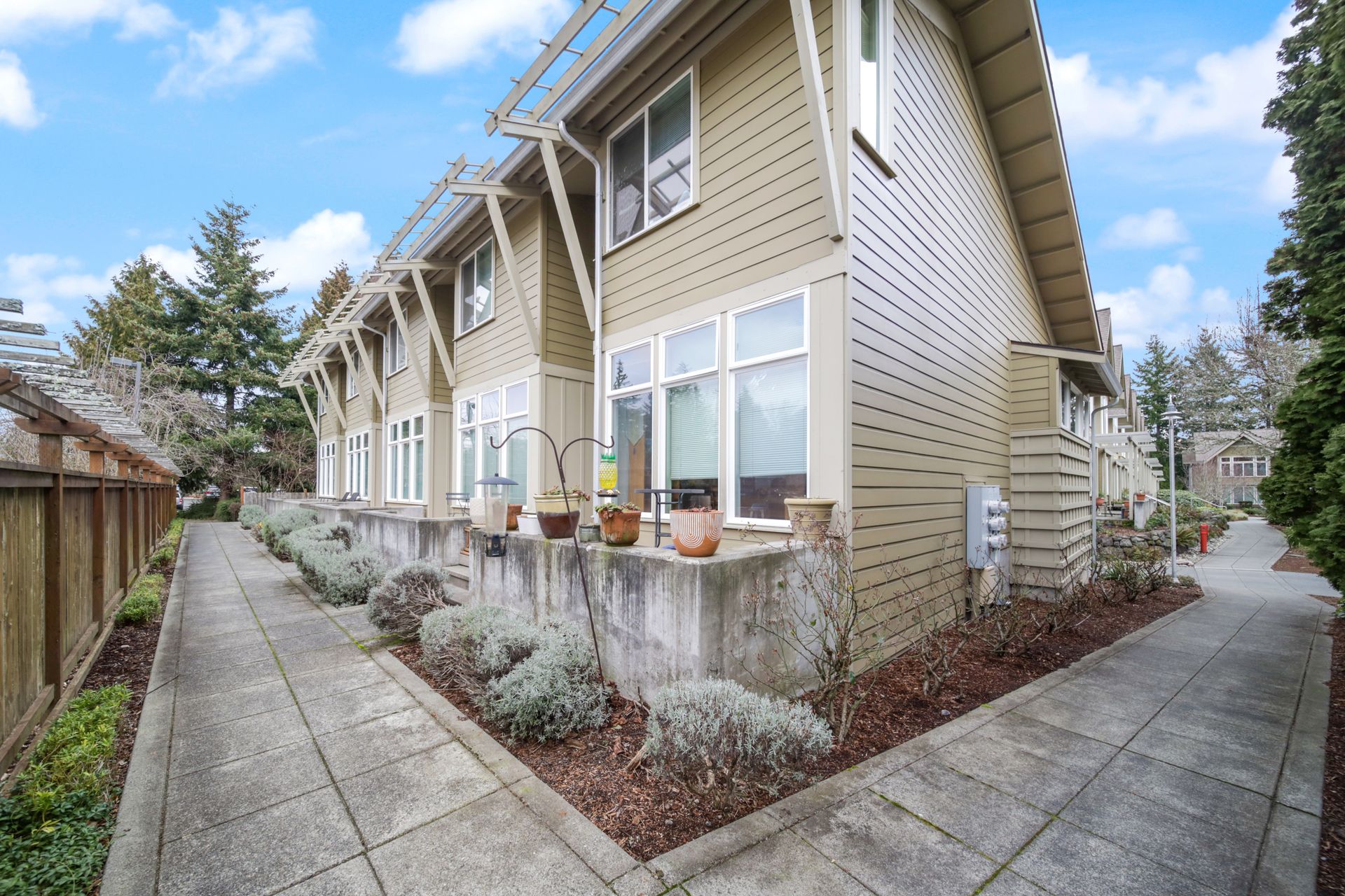 Exterior of a beige townhouse row with front walkway, windows, and small landscaped beds