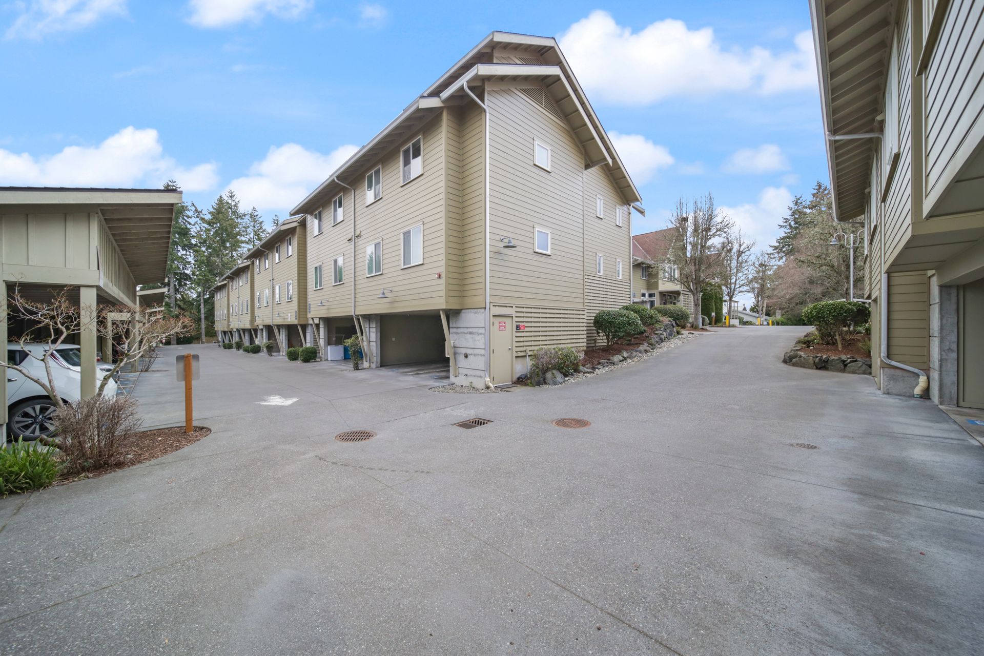 Apartment complex courtyard with beige buildings, gravel driveways, and a covered parking area under a blue sky