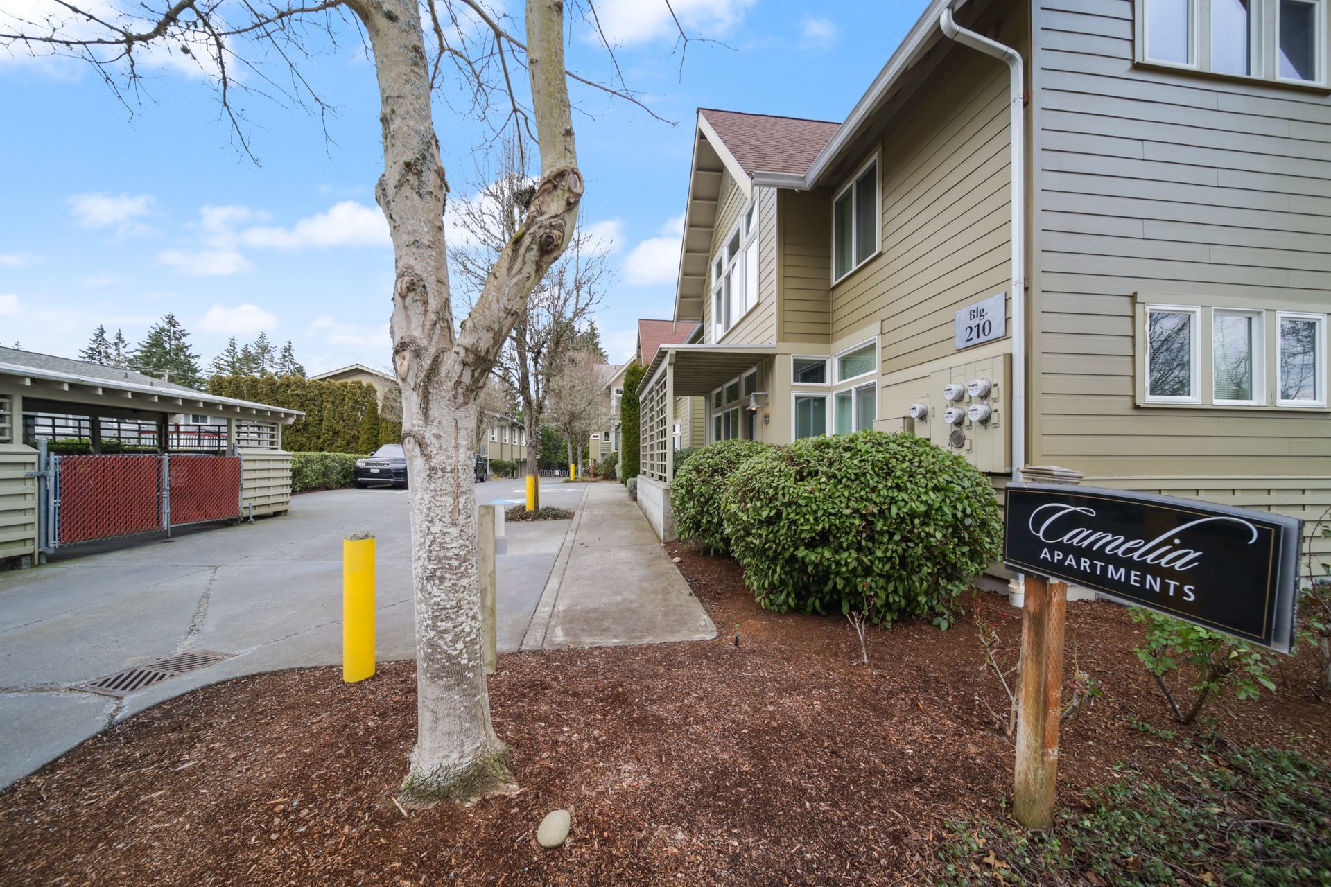 Exterior of beige building with sidewalk, trees, and a black sign by the entrance