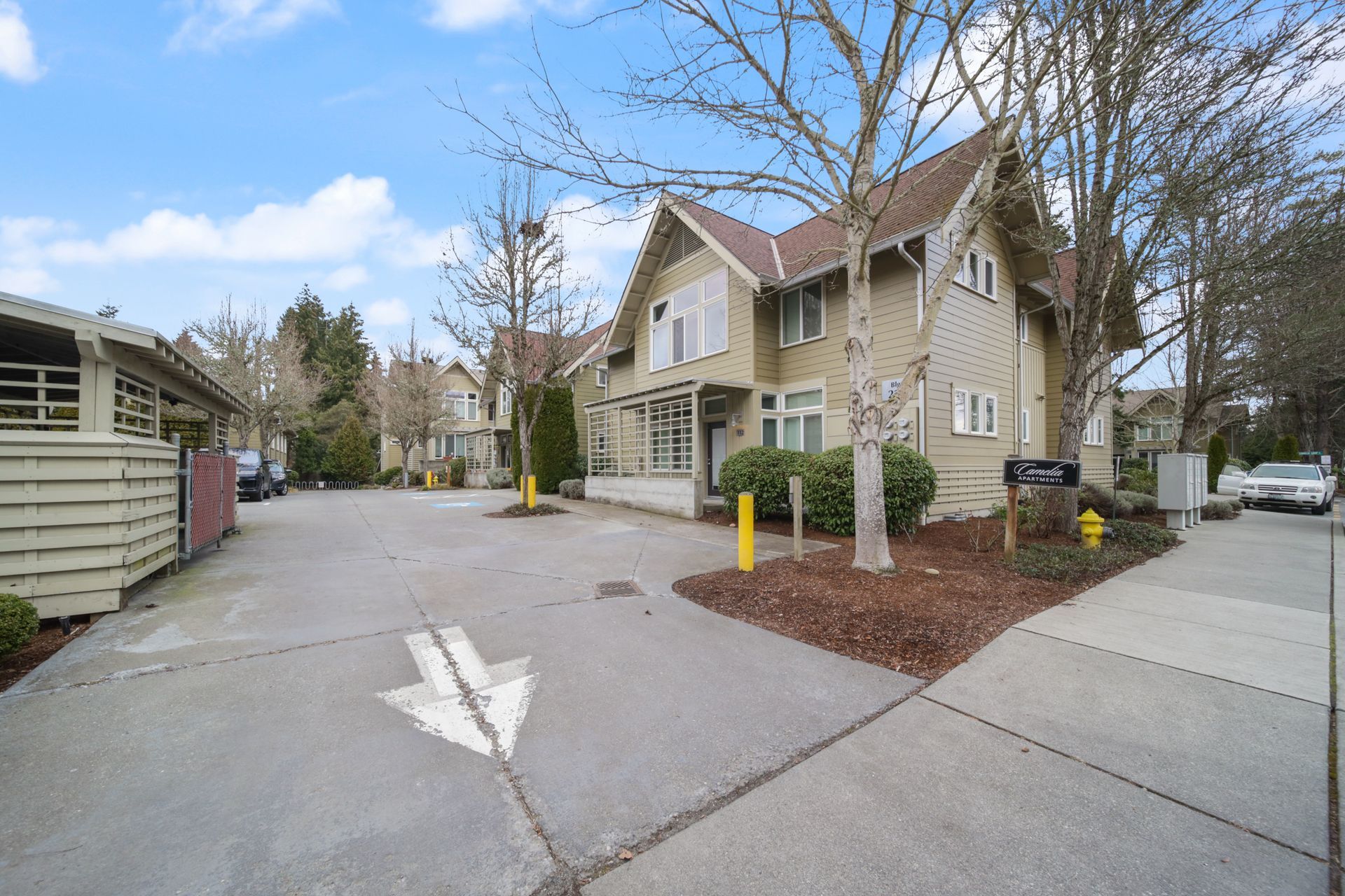 Residential street with townhouses, driveway, sidewalk, and a yellow bollard under bare trees