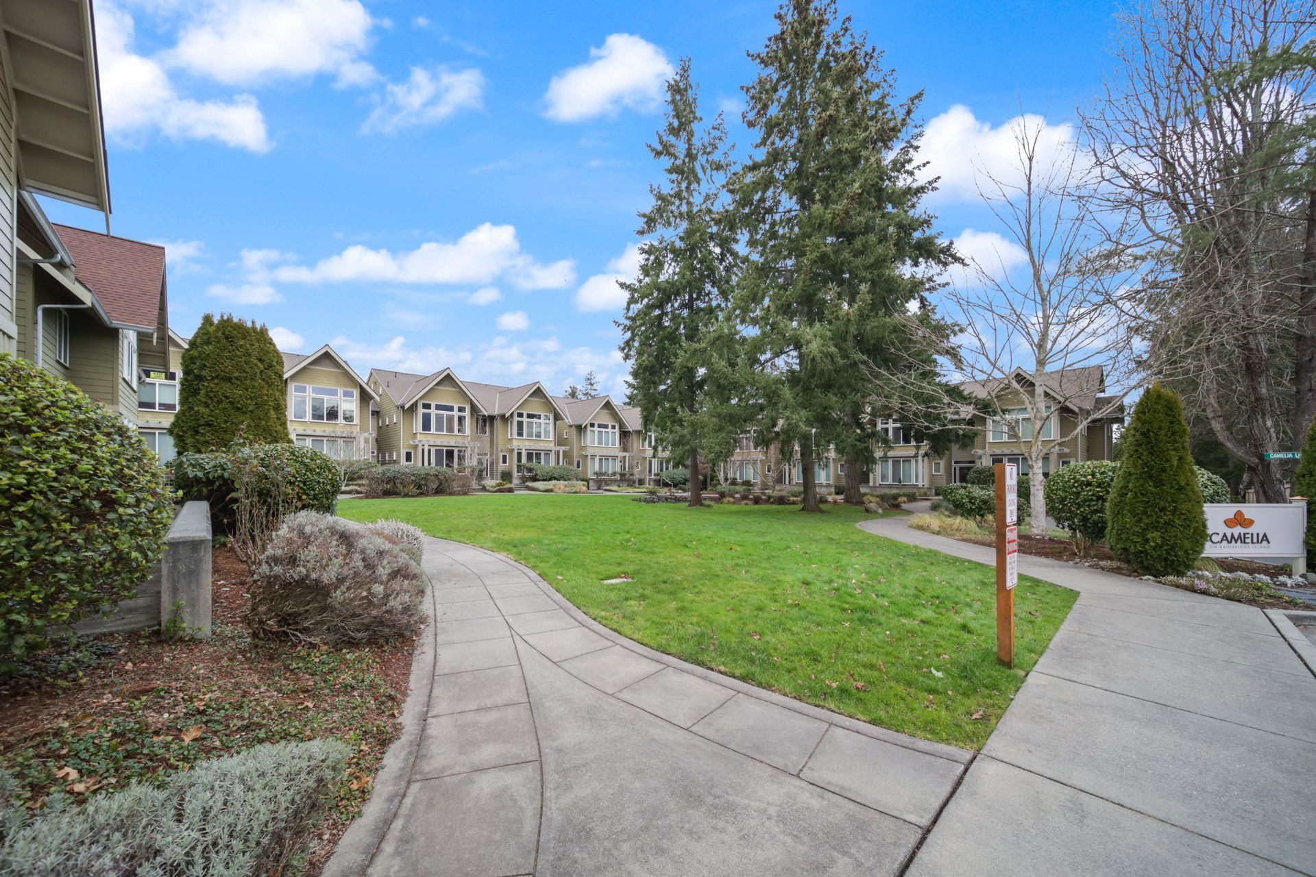 Curved sidewalk beside a green lawn and townhouses under a blue sky with clouds