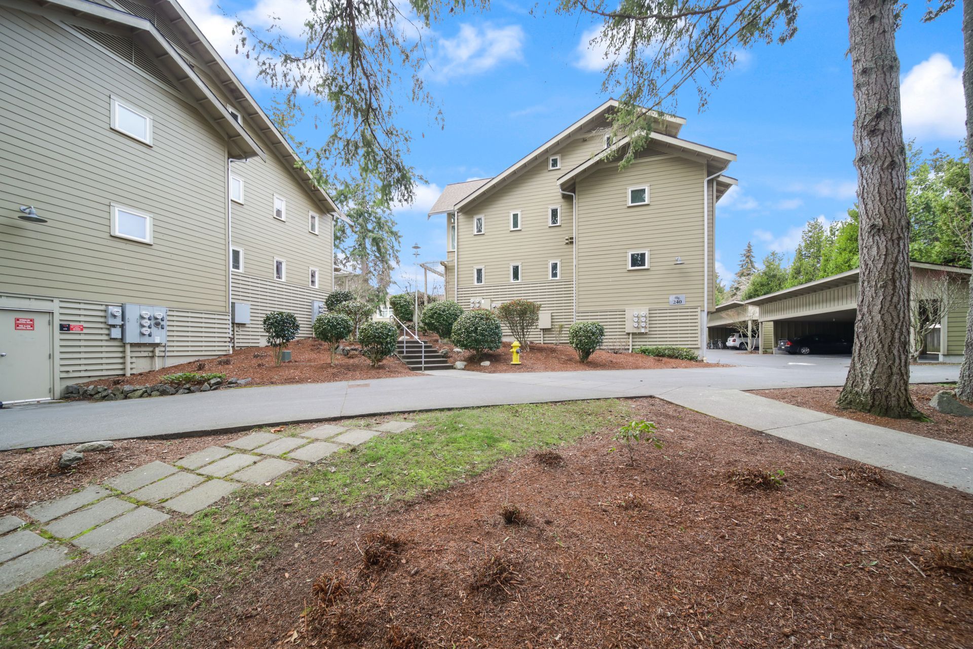 Apartment buildings with sidewalks, trees, and a landscaped courtyard under a partly cloudy sky