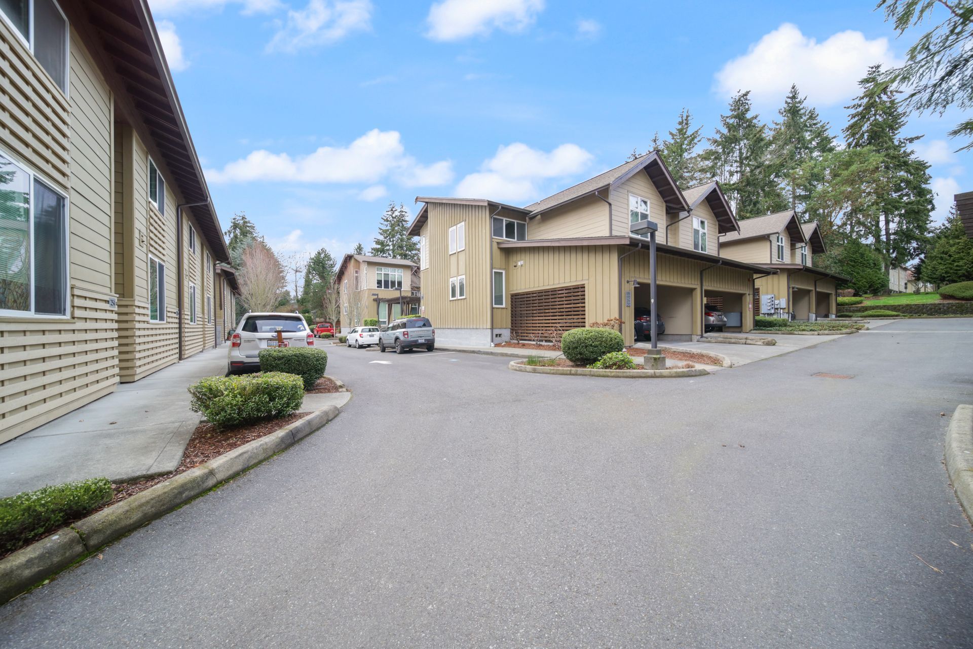 Residential apartment complex with tan buildings, paved driveway, and parked car under a blue sky