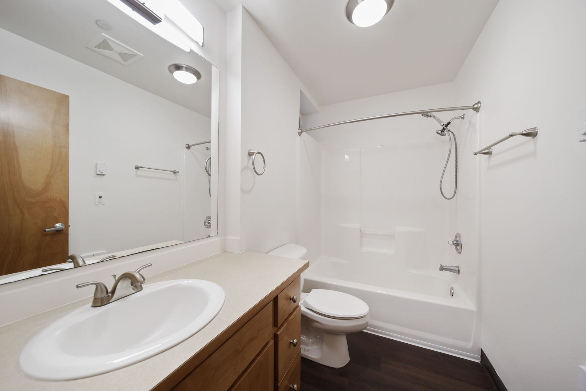 Bright bathroom with sink vanity, mirror, toilet, and shower/tub combo with white walls and dark floor.