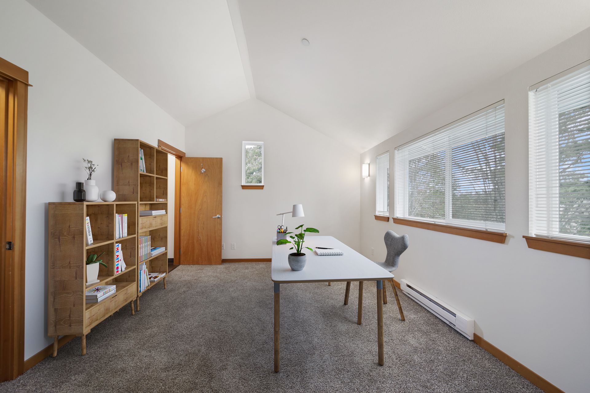 Bright home office with a table, chair, shelves, and large windows along a sloped wall.