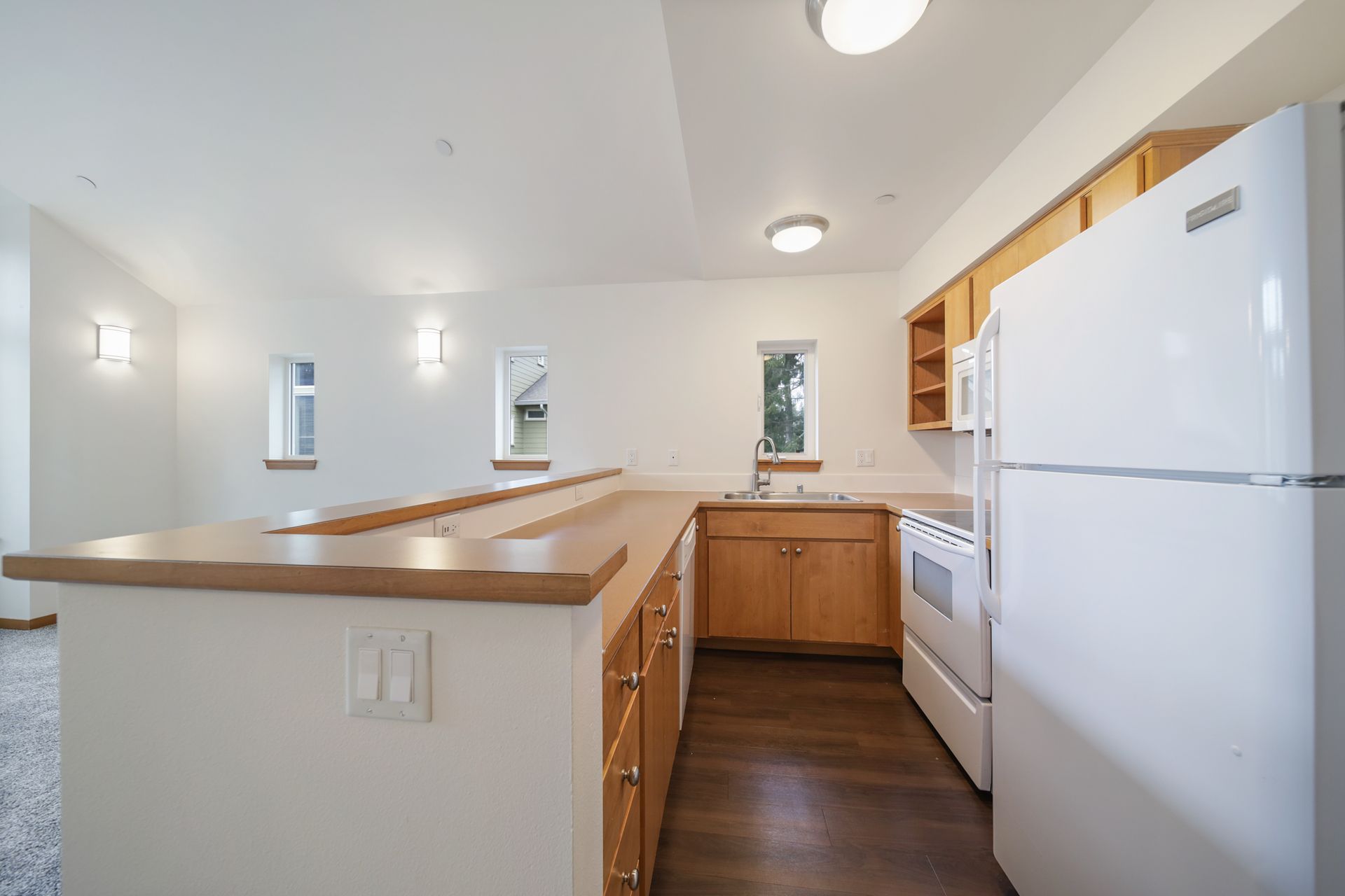 Bright kitchen with white appliances, wood cabinets, and a peninsula counter under recessed lights