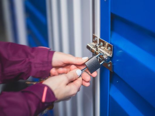 Hands locking a blue storage unit door with a padlock