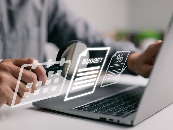 Hands typing on a laptop with floating budget and percentage icons on screen