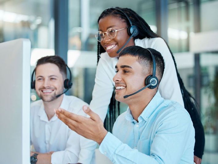 Three customer support agents wearing headsets working together in a bright office