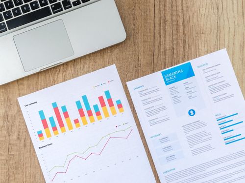 Laptop on desk beside printed business charts and reports with colorful graphs and data tables
