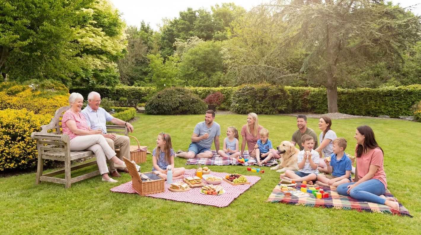 Group enjoying a picnic on blankets and bench in a sunny garden with flowers and trees
