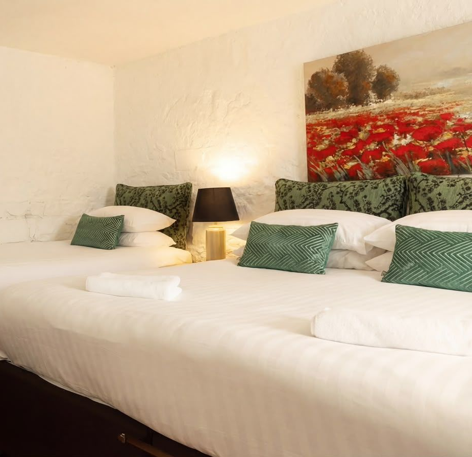 White bed with green pillows, bedside lamp, and floral wall art in a bright bedroom