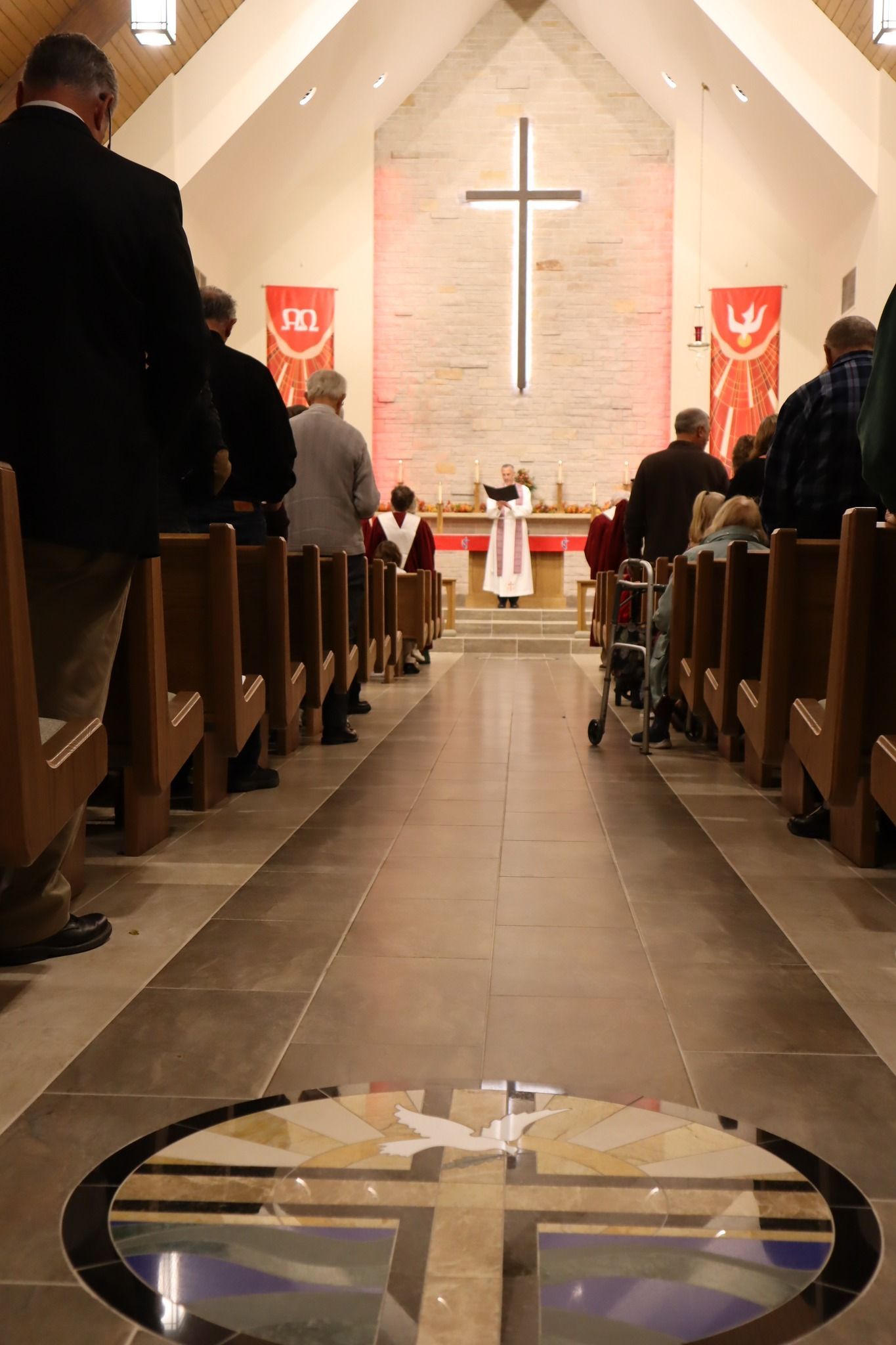 Congregation seated in a church aisle facing a cross-lit altar during a service