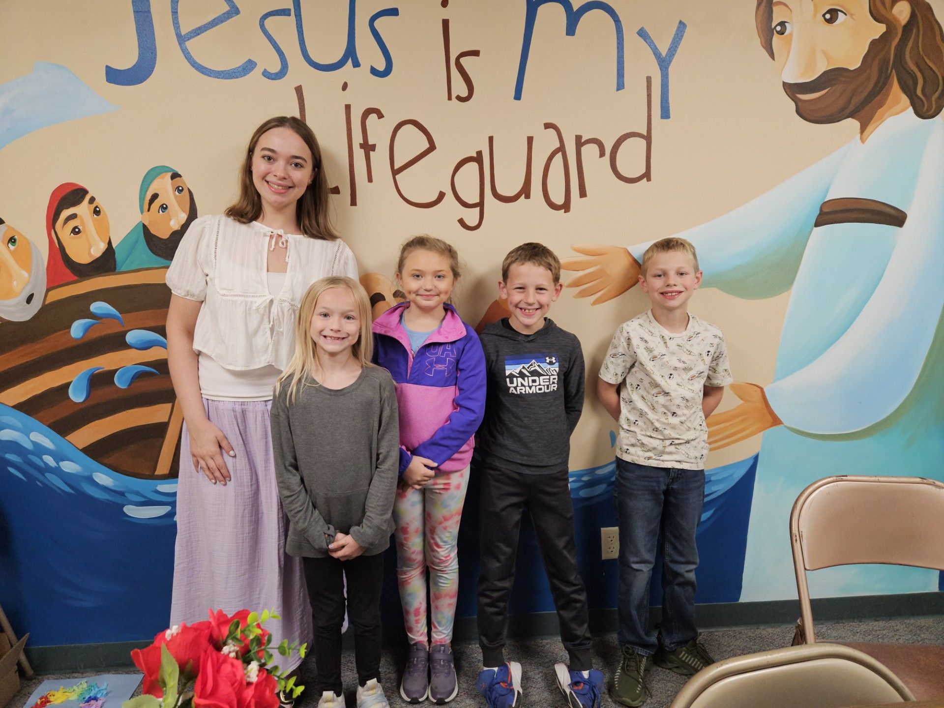 Woman and four children posing in front of a mural reading “Jesus is my lifeguard”