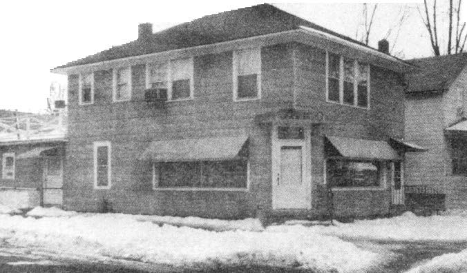 Snowy exterior of a two-story brick house with a side addition and bare trees nearby