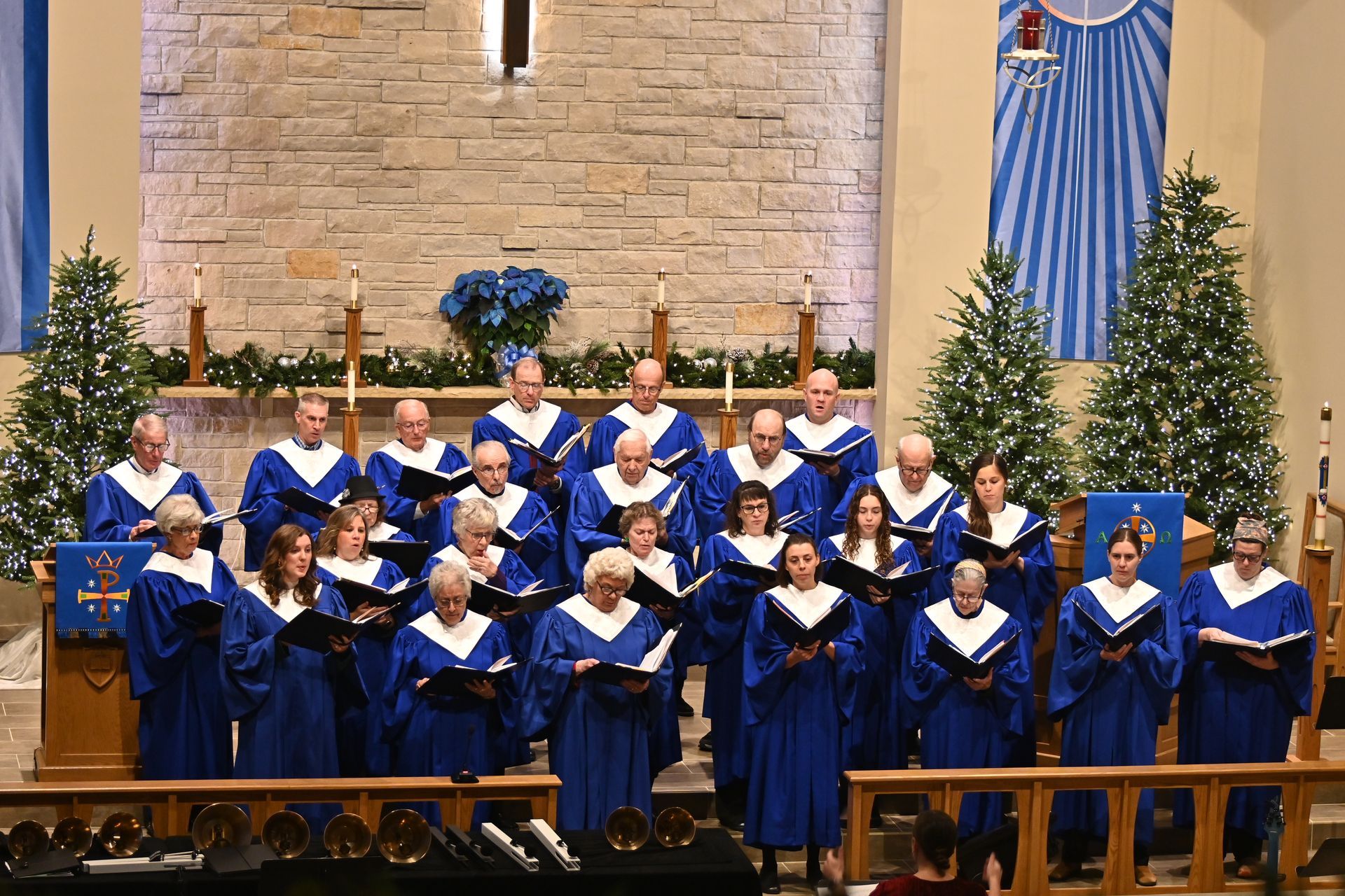 Choir in blue robes singing in front of a church altar with decorated Christmas trees and blue banners
