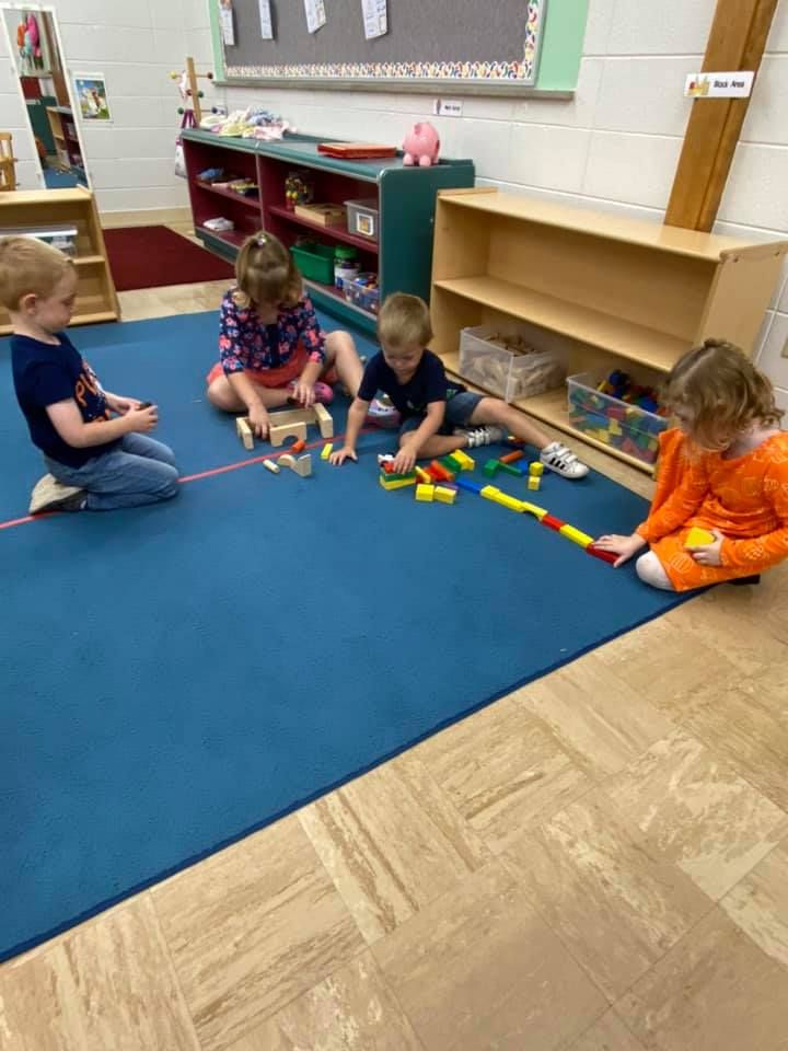 Children sitting on a classroom rug building with colorful blocks and wooden toys