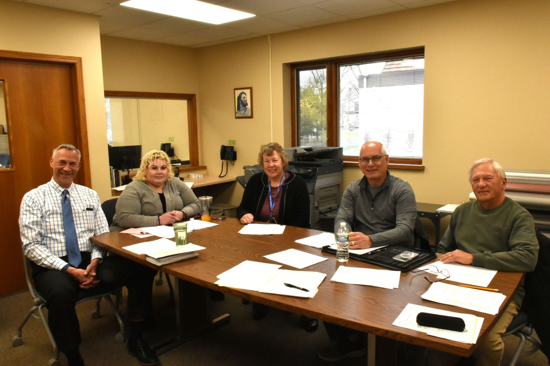 Five people seated around a conference table in a meeting room, with papers and a phone on the table.