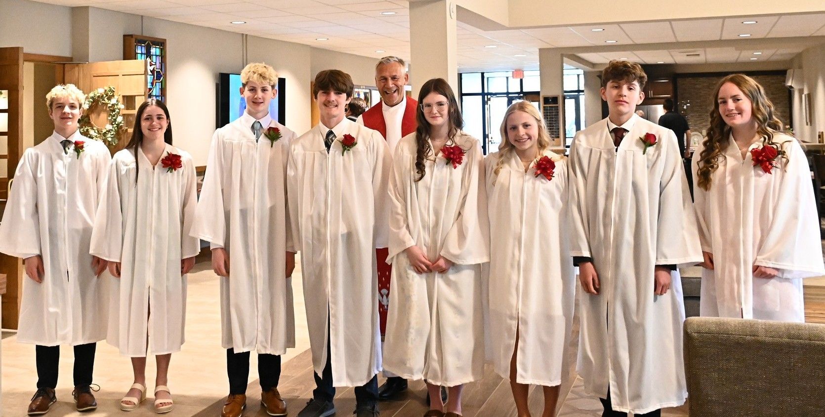 A choir group in white robes stands indoors in a church or hall, posing for a photo.