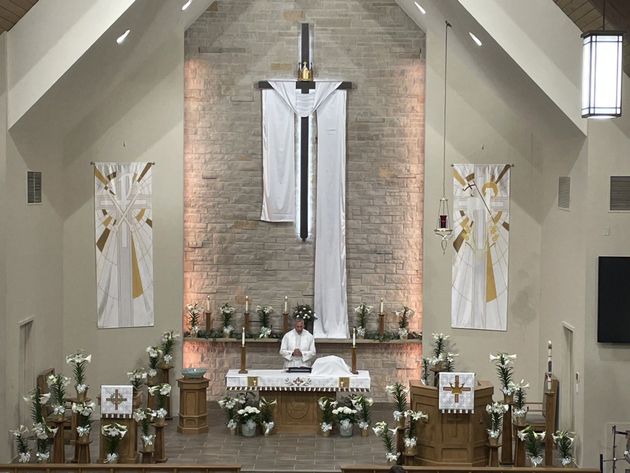 Church altar with white drapery, candles, flowers, and a priest standing at the center.