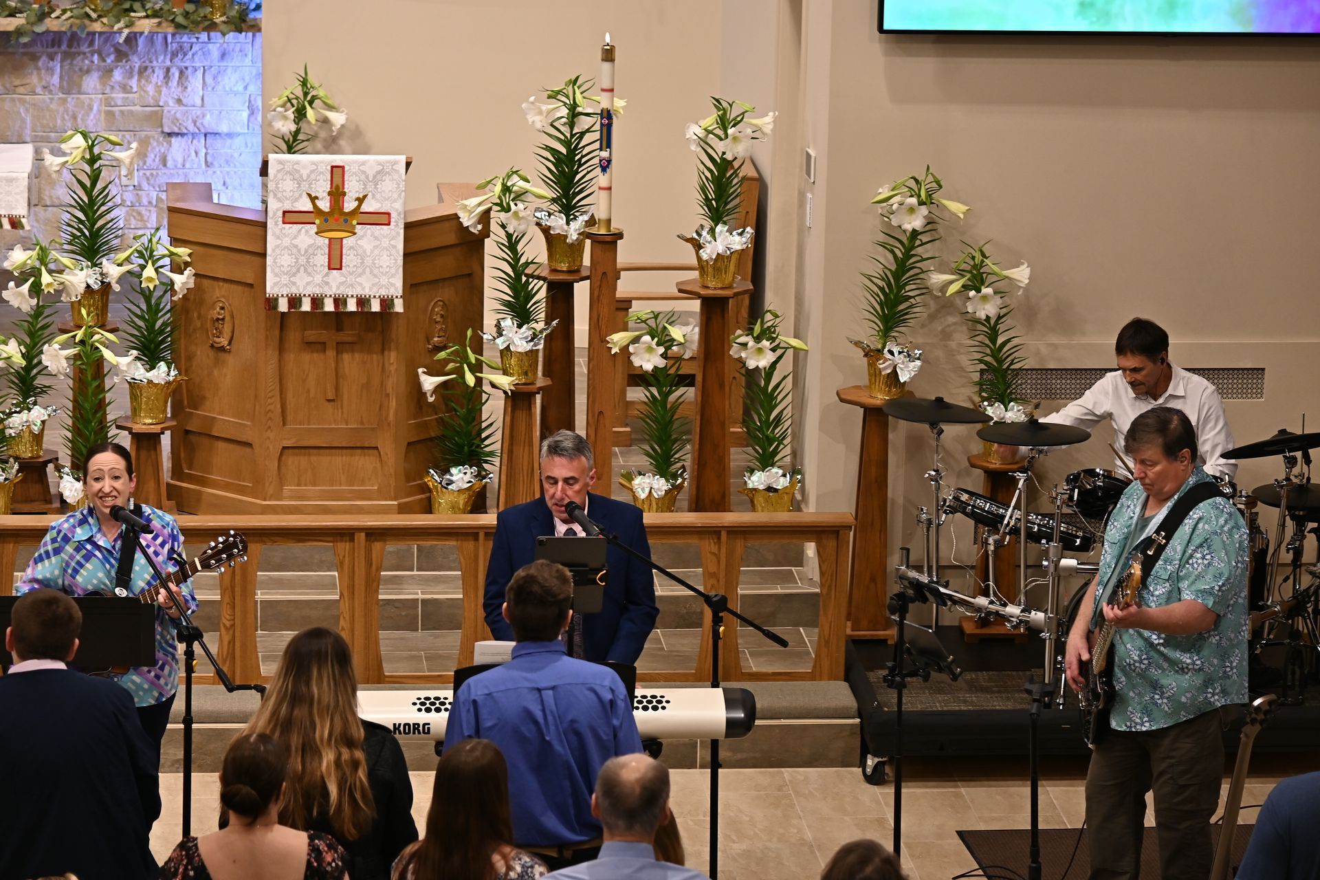 Musicians performing in a church sanctuary, with a drummer, singer, guitarist, and audience seated in front