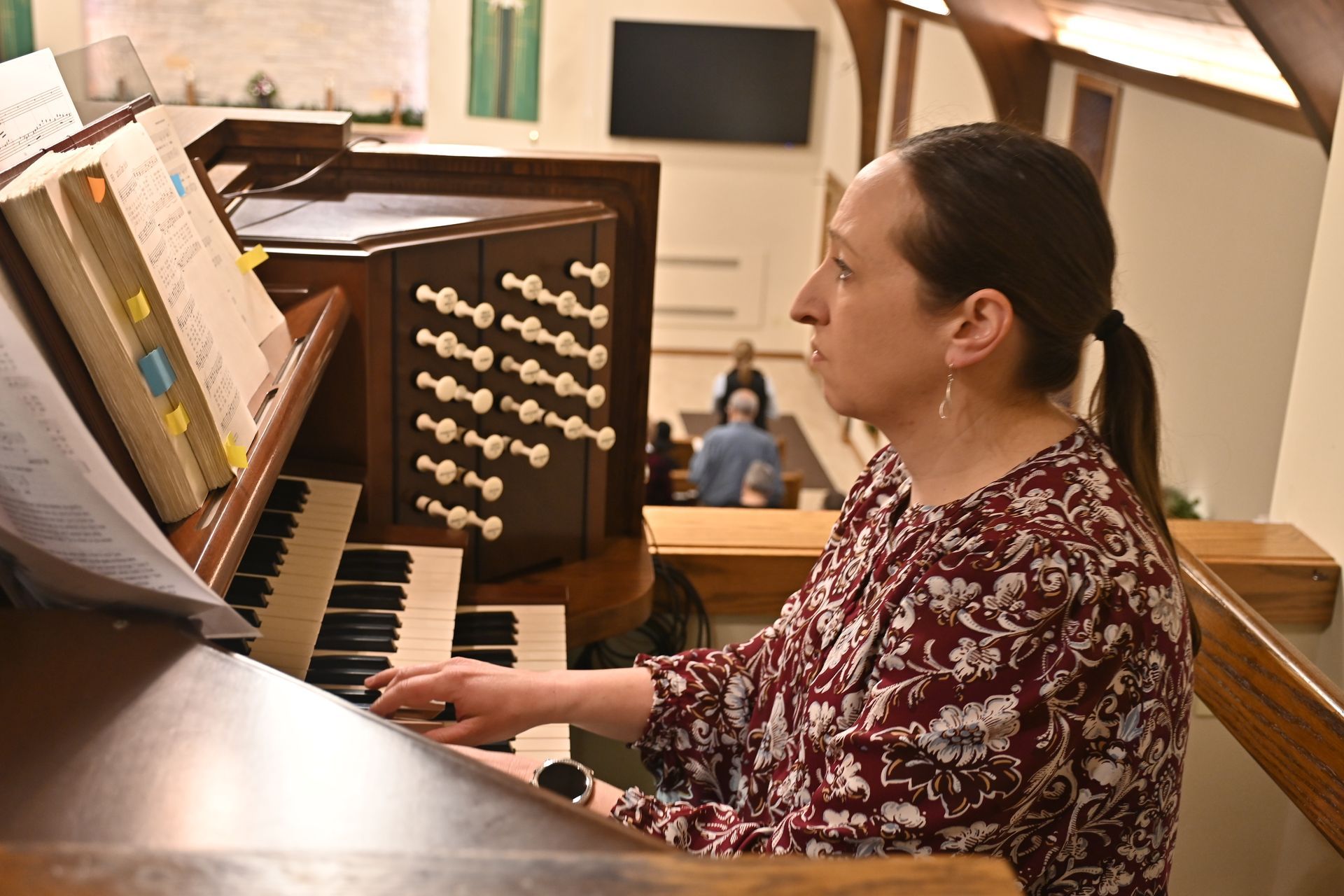 Woman playing a pipe organ in a church, seated at the console with sheet music visible.