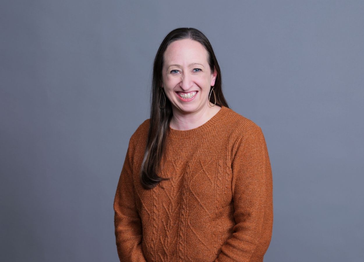 Smiling woman in a brown sweater against a gray background
