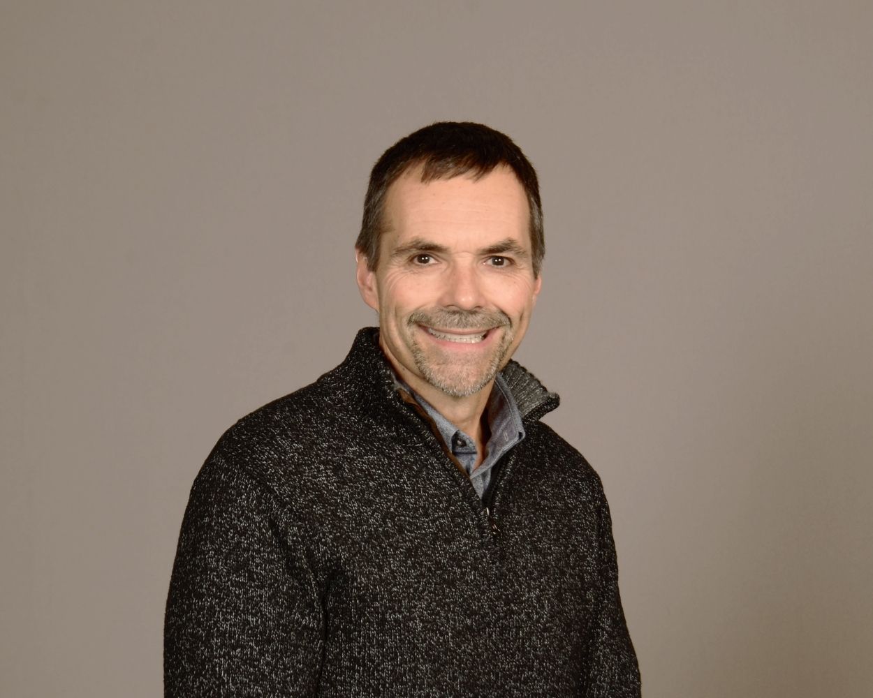 Smiling man in a dark sweater against a plain gray background