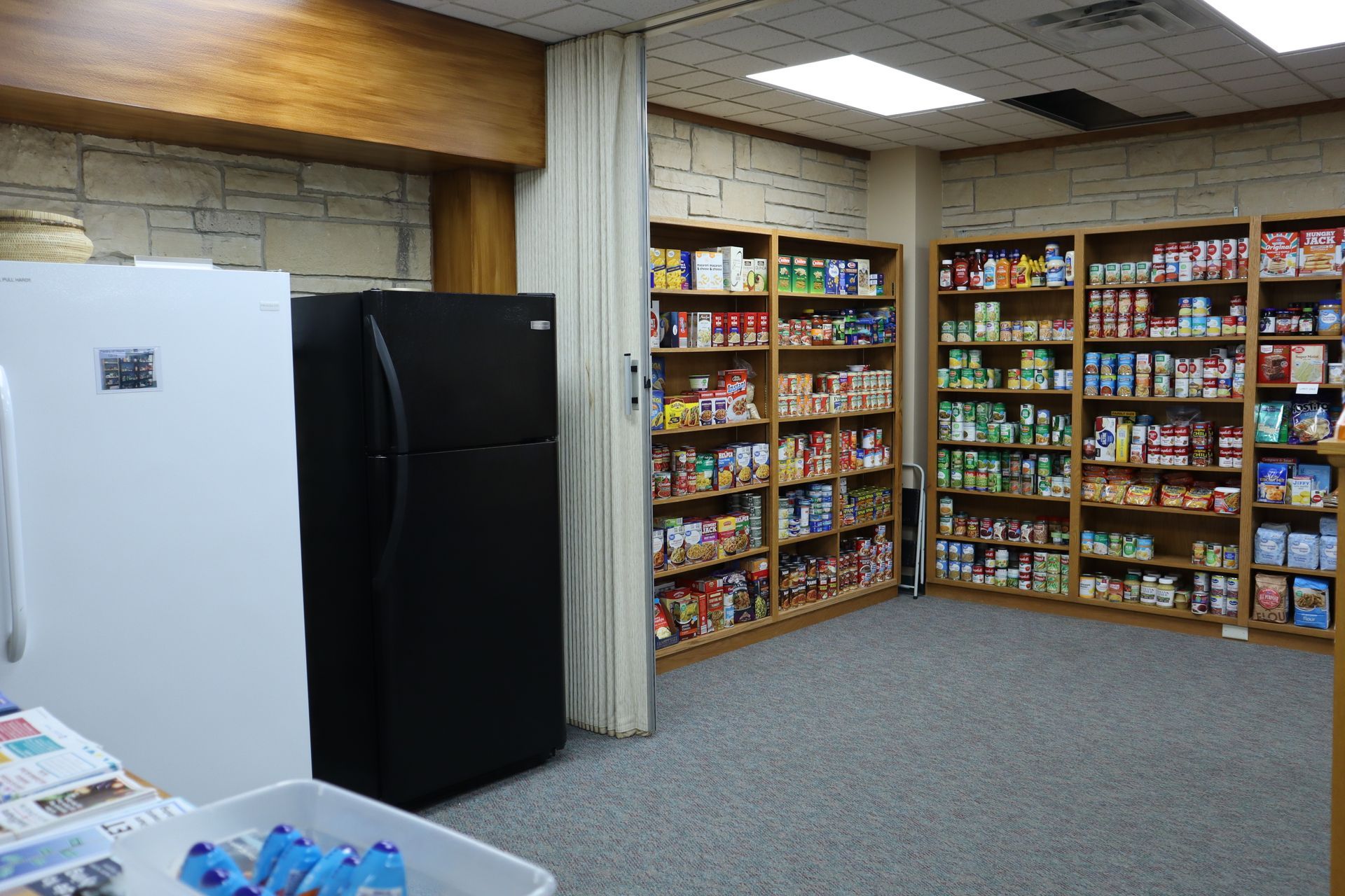 Small room with shelves of colorful snacks and drinks, plus white and black refrigerators along the wall.