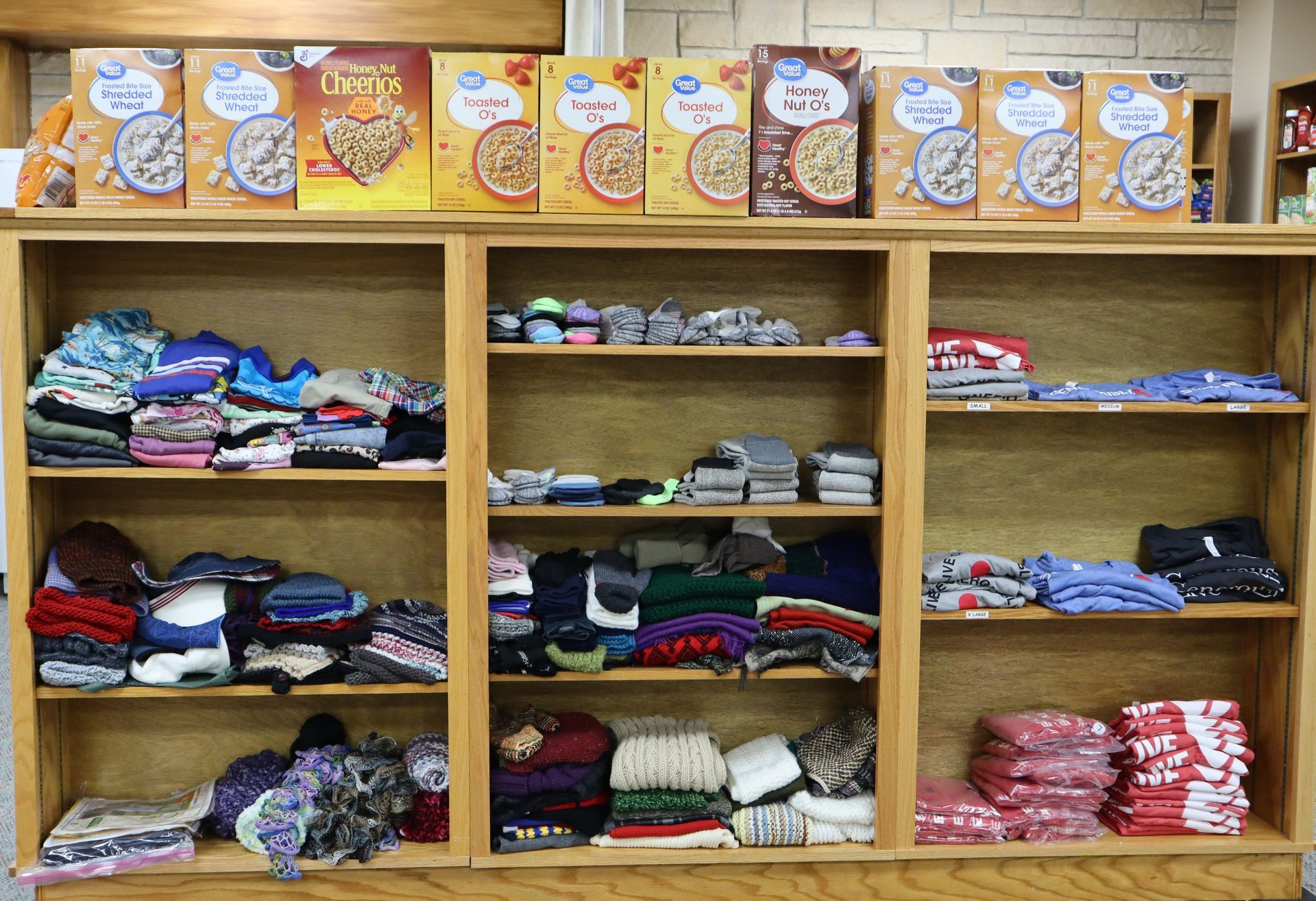 Shelves of folded clothes in a store, with decorative cards displayed along the top.