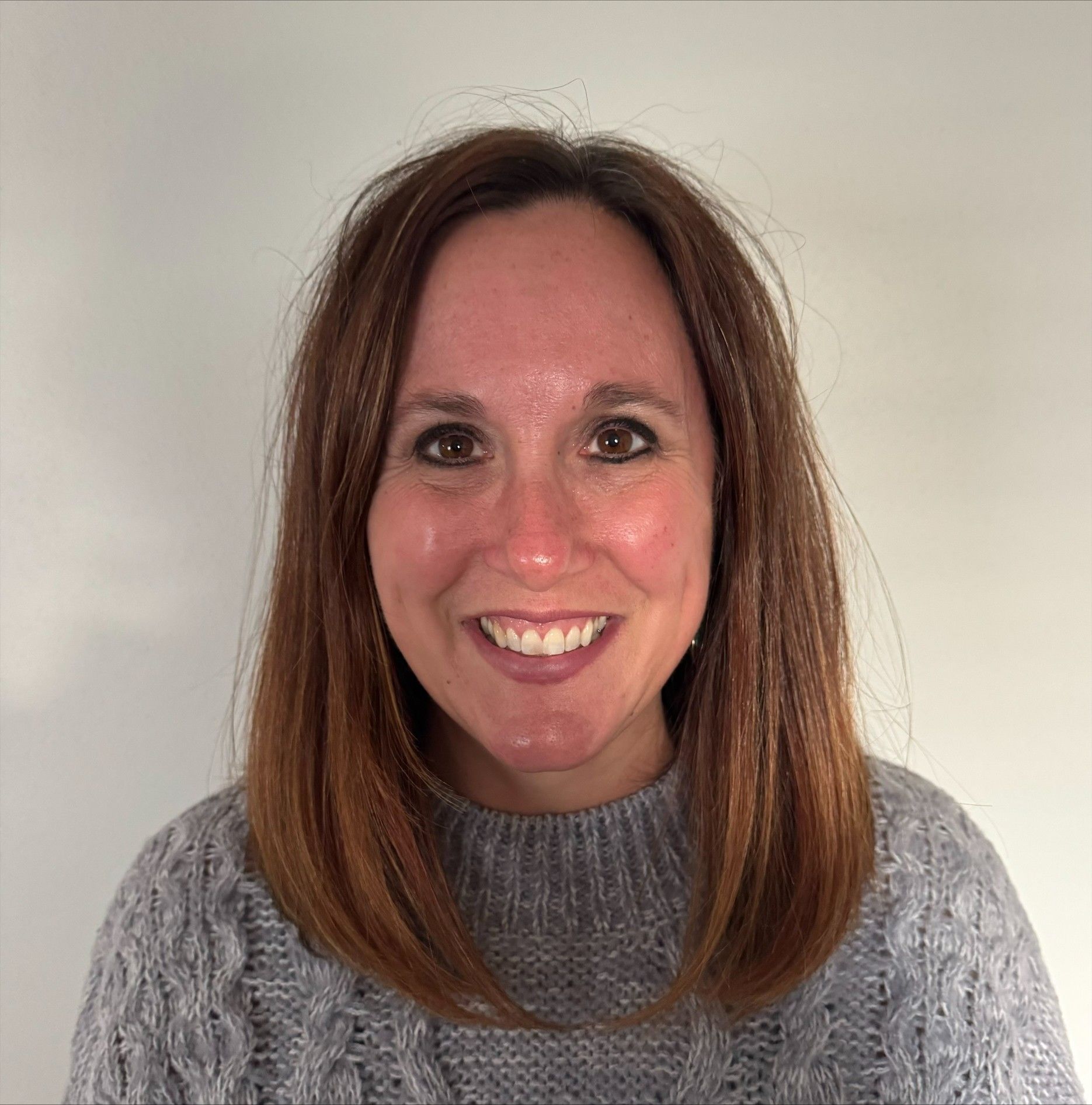 Smiling woman with shoulder-length brown hair wearing a gray sweater against a plain light background